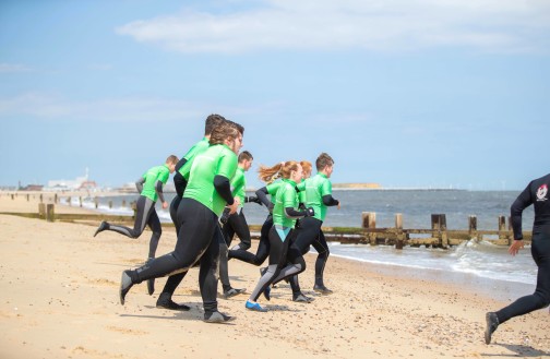 Outdoor Leadership cohort in surfing gear, running into the sea from the shore 